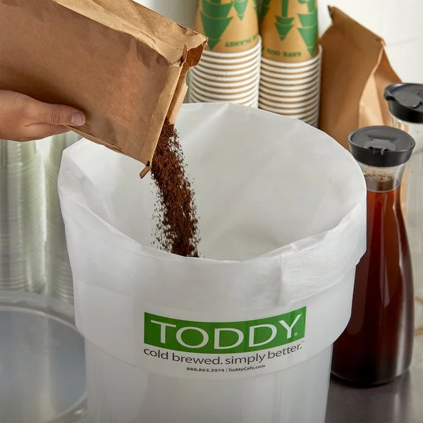 Pouring coffee into a paper filter in a plastic container for Toddy Commercial Cold Brew preparation.