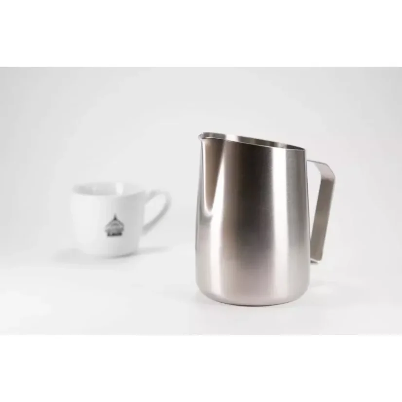 Cafetière en acier inoxydable pour faire mousser le lait, posée sur une table blanche accompagnée d'une tasse en porcelaine.