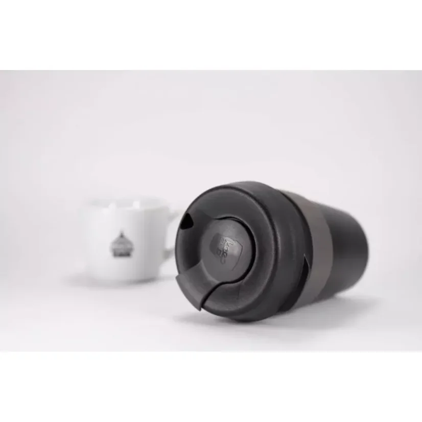 Thermos noir en plastique avec un support gris posé sur une table blanche, fond blanc.