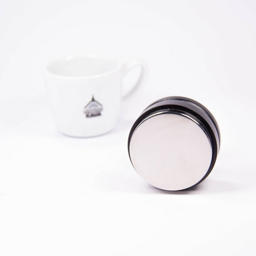 View of the bottom of the push tamper, on the left a cup with the logo of Spa Coffee.