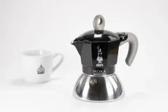 Alumīnija moka kafijas tējkanna, piemērota indukcijai ar ražotāja - itāļu uzņēmuma Bialetti logotipu, kompozīcijā ar krūzi.