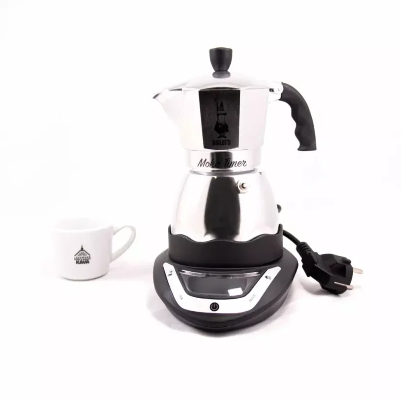 Strieborná moka kanvička značky Bialetti Moka Timer pre 3 šálky na čiernom podstavci a v pozadí položený biely šálka s motivmi.