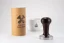 Heavy Temper with a diameter of 58 mm and a black handle on a white table with a cup of coffee and the original packaging for the temper.
