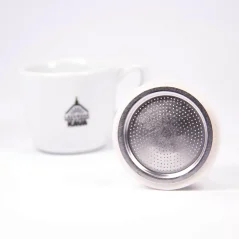 Joint en aluminium argenté pour cafetière moka Bialetti reposant sur un bord sur fond blanc avec une tasse ;