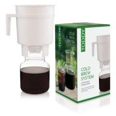 Toddy Cold Brew üveg rendszer, műanyag szűrőtartállyal és átfolyt kávéval, az eredeti doboz mellett fehér háttéron.