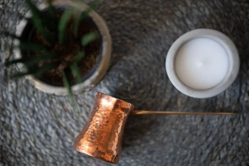 Copper coffee pot, a flower in a pot, and a bowl of sugar on a woven placemat