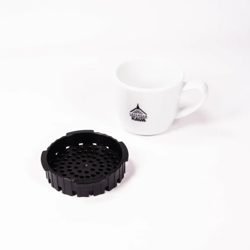 Schwarzes Aeropress-Kaffeefiltersieb auf weißem Hintergrund mit einer Tasse Kaffee.