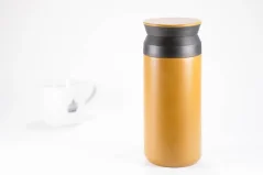 Stainless steel brown Kinto thermos bottle, 350 ml volume, on a white background with a cup of coffee