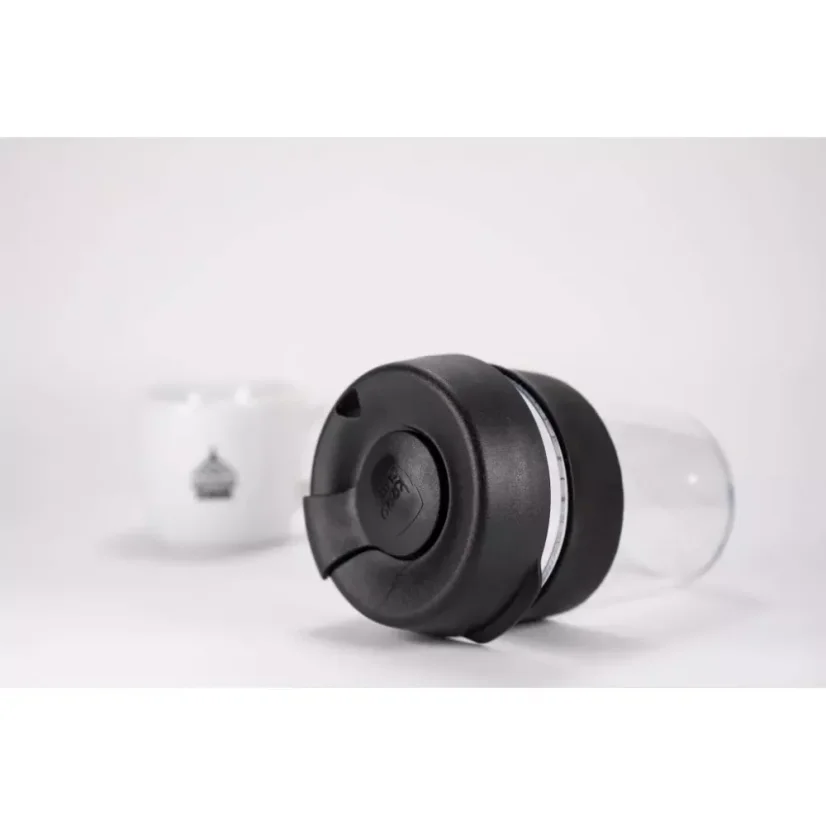 Gobelet thermos en plastique posé sur une table blanche à côté d'une tasse blanche.