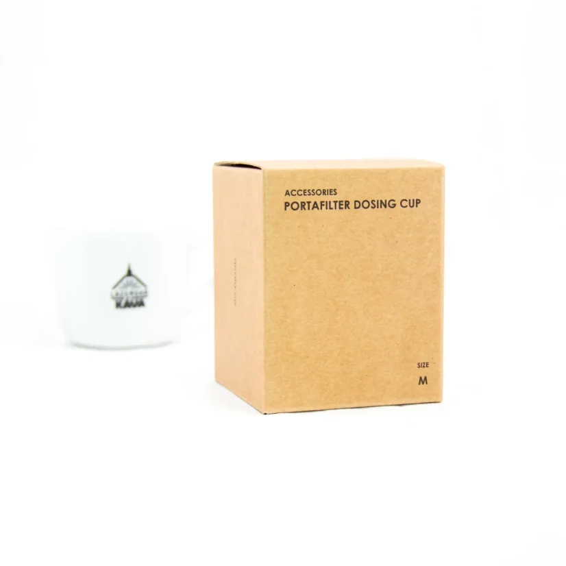Paper box for stainless steel Acaia Dosing Cup M in front of a cup with a logo on a white background